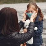 Woman in a disposable mask is teaching her child to wear a respirator